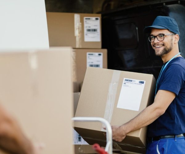 young-happy-manual-worker-carrying-cardboard-boxes-delivery-van-while-communicating-with-his-colleagues (1)